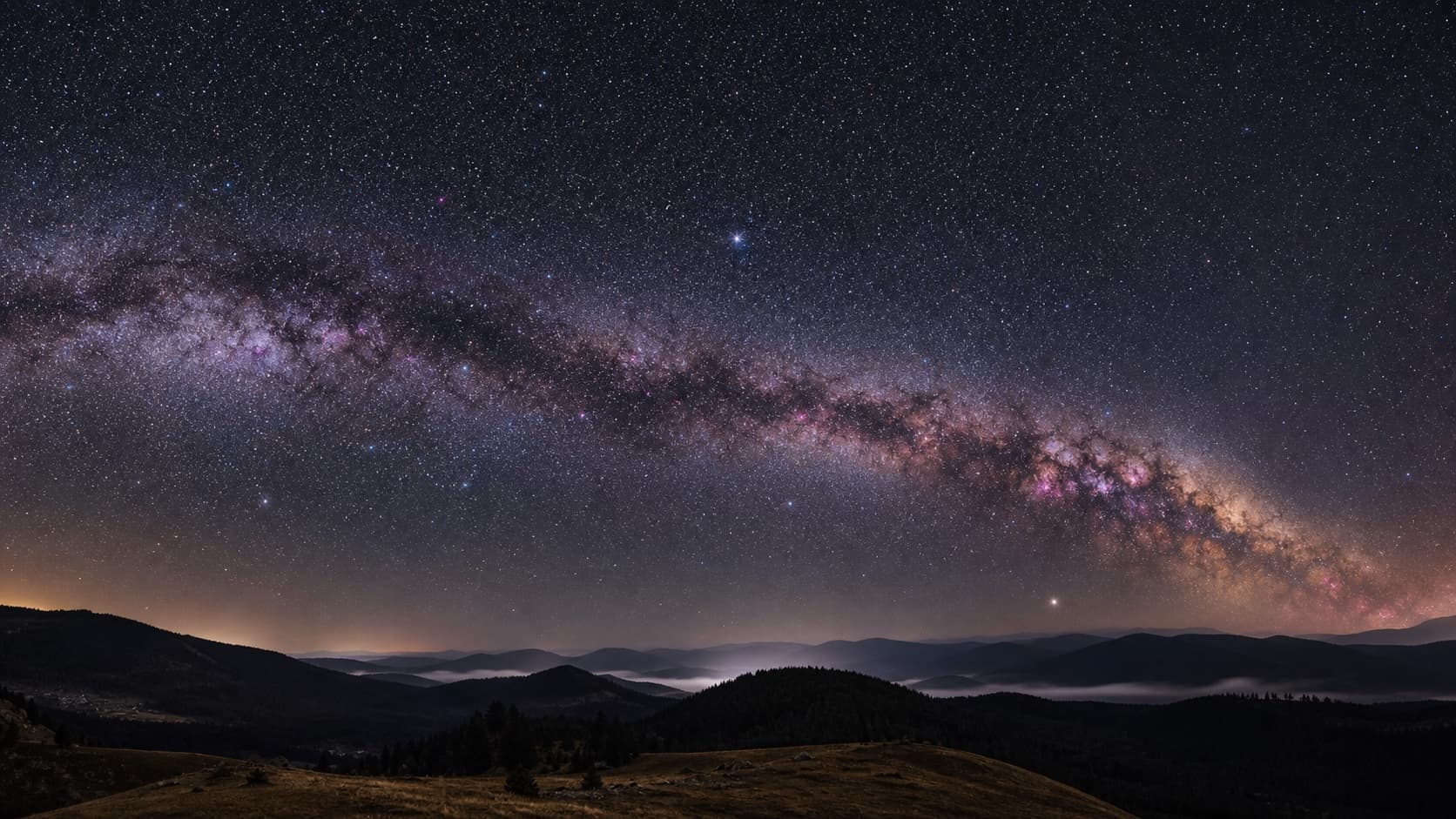 The Milky Way arching over rolling hills under a starry sky