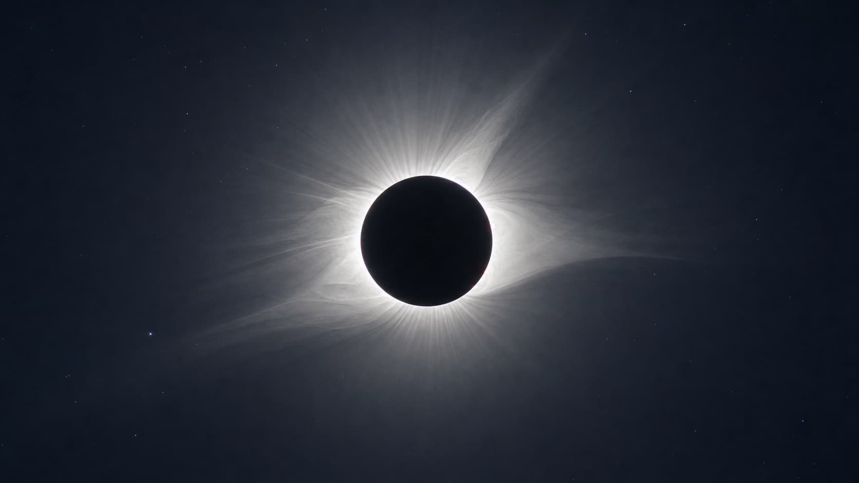 A total solar eclipse with the white corona ringing a dark moon.