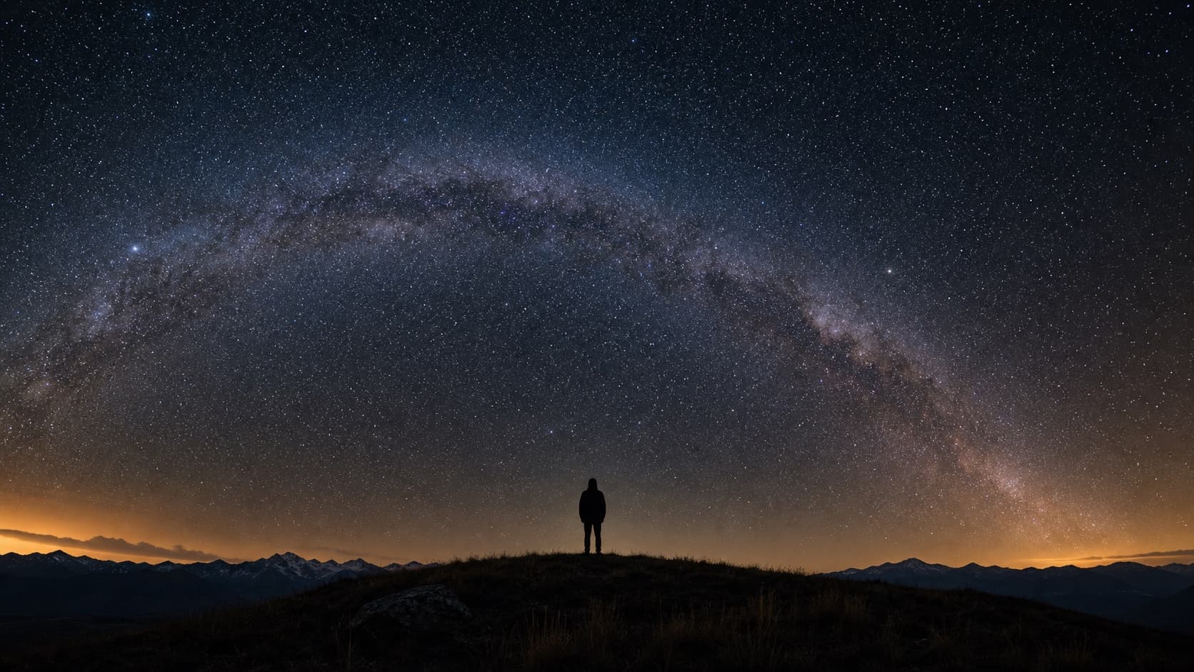 A person's silhouette beneath a sky full of stars at night.
